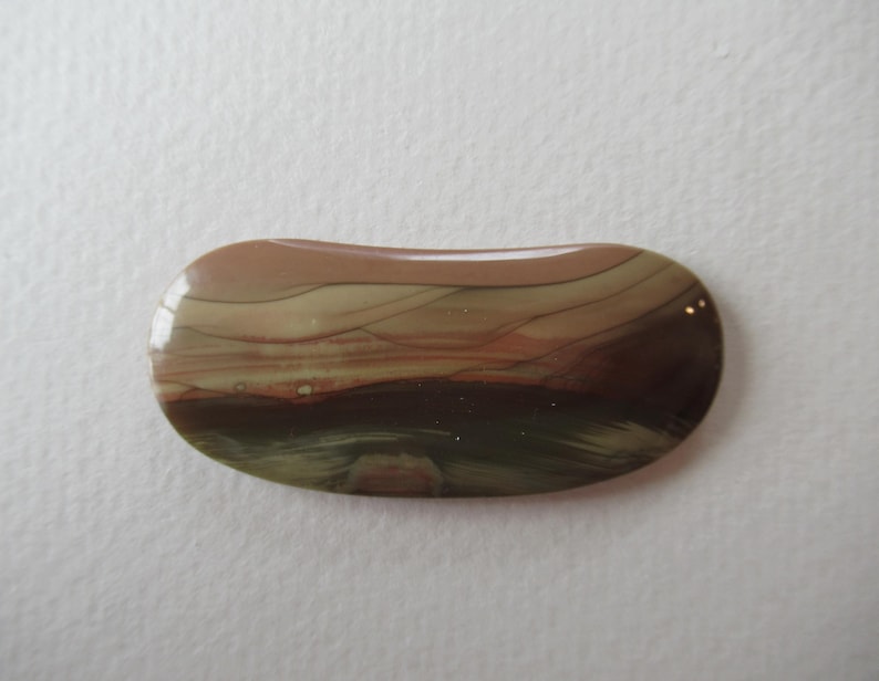 May include: A polished, oval-shaped gemstone with a layered pattern of brown, tan, and green hues. The stone has a glossy finish and a smooth, rounded shape. The colors blend together, creating a natural, earthy aesthetic.