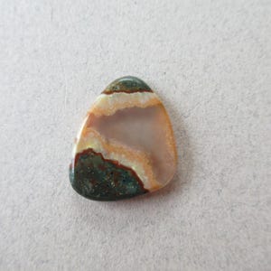 May include: A teardrop-shaped cabochon of green, brown, and white agate with a layered pattern.