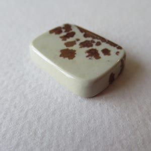Pode incluir: Um caboch&atilde;o de pedra branco e marrom salpicado com uma superf&iacute;cie lisa e polida.