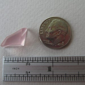 May include: A pale pink, faceted gemstone next to a U.S. dime and a ruler. The gemstone has a geometric shape. The ruler shows inch measurements. The dime is dated 1956.