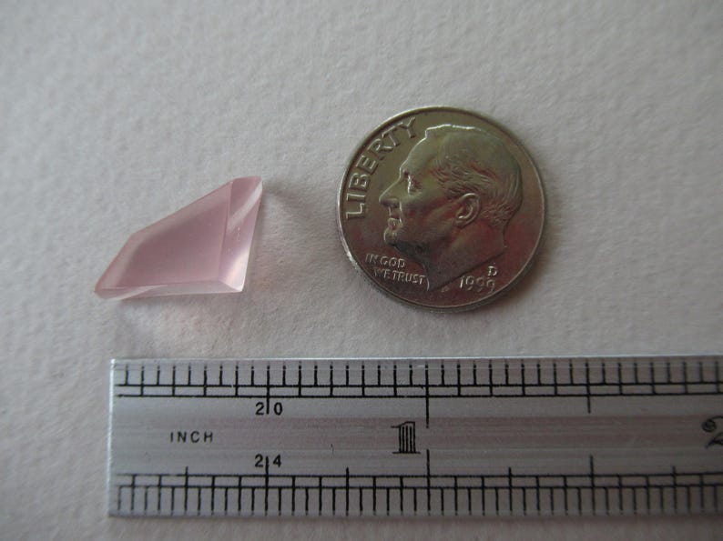May include: A pale pink, faceted gemstone next to a U.S. dime and a ruler. The gemstone has a geometric shape. The ruler shows inch measurements. The dime is dated 1956.