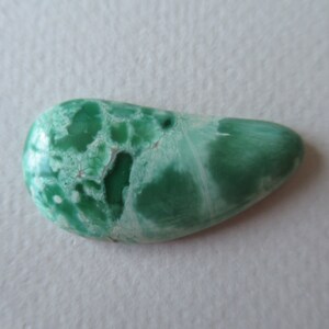 May include: A polished, teardrop-shaped gemstone with a mottled pattern of green and white. The stone's surface has a smooth, glossy finish, and the colors blend together in a natural, organic design. The gemstone is a unique, handcrafted item.