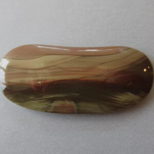 May include: A polished, oval-shaped stone with a glossy finish. The stone features a blend of colors, including shades of brown, beige, and dark red, with a layered, banded pattern. The overall shape is smooth and rounded.