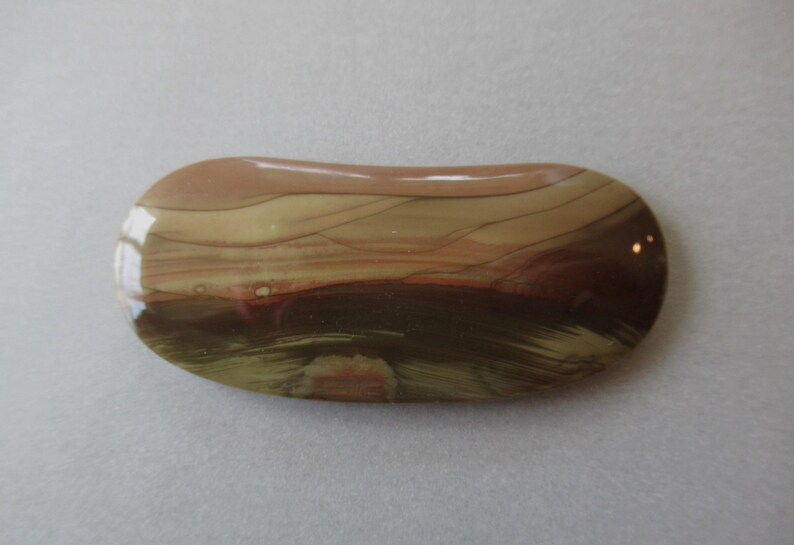 May include: A polished, oval-shaped stone with a glossy finish. The stone features a blend of colors, including shades of brown, beige, and dark red, with a layered, banded pattern. The overall shape is smooth and rounded.