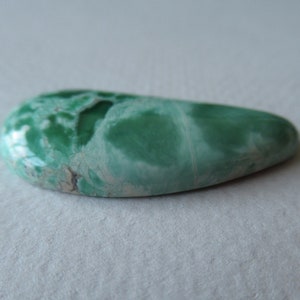 May include: A polished, teardrop-shaped gemstone with a vibrant green hue, featuring a marbled pattern of lighter green and white. The stone has a smooth, glossy surface, ideal for jewelry or collection.