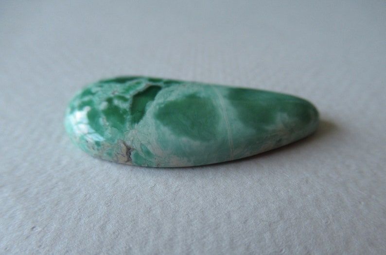 May include: A polished, teardrop-shaped gemstone with a vibrant green hue, featuring a marbled pattern of lighter green and white. The stone has a smooth, glossy surface, ideal for jewelry or collection.