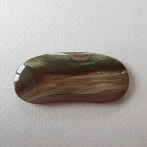 May include: A polished, oval-shaped gemstone with a mix of colors. The stone features bands of brown, tan, and green, creating a natural, earthy pattern. The surface is smooth and reflective, suggesting a high-quality finish.