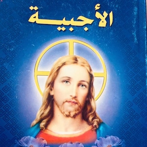 May include: A book cover with the Arabic text "الأجبية" in gold lettering. The image features a portrait of Jesus with long hair and a beard, surrounded by a golden halo. Blue roses are at the bottom.