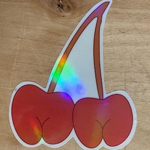 May include: A sticker of two red cherries with a green stem. The sticker has a holographic finish.