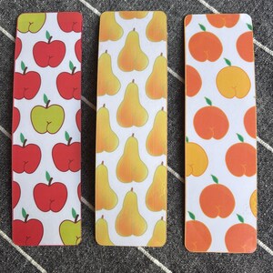 May include: Three bookmarks with different fruit patterns. The first bookmark has a red apple pattern, the second bookmark has a yellow pear pattern, and the third bookmark has an orange peach pattern.
