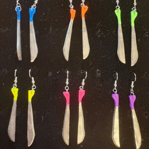 May include: A collection of handmade earrings with silver-colored hooks and blades. The blades are painted with various colors, including blue, orange, green, yellow, pink, and purple. The earrings are displayed against a dark background.