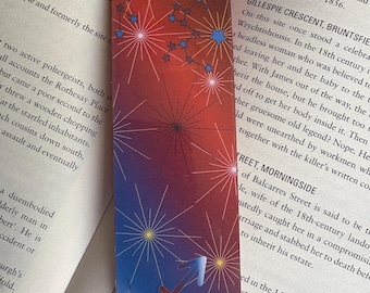 May include: A colorful bookmark with a red, orange, and blue gradient background. The bookmark features a white starburst design and a white silhouette of the Sagittarius zodiac symbol. The bookmark also includes text that reads "Royal Lyceum Theatre, London" and "Gillespie Crescent, Bruntsfield".