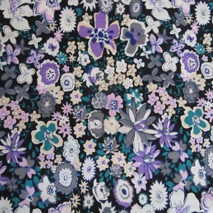 Op de afbeelding: Zwarte stof met een bloemenprint met verschillende bloemen in tinten van paars, roze, wit en turquoise.