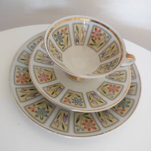 Peut inclure: Un ensemble de trois tasses à thé et soucoupes en porcelaine blanche avec un motif floral. Les tasses et les soucoupes ont une bordure dorée et présentent un motif répétitif de fleurs bleues, rouges et jaunes.