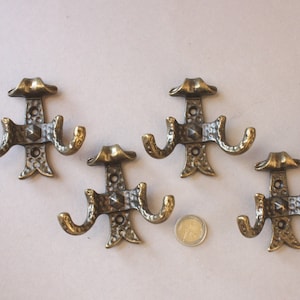 May include: Set of six antique brass hooks with a decorative design. Each hook has three prongs and a decorative top.