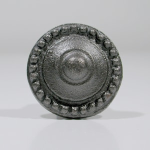 May include: A round, silver-colored metal knob with a beaded border and a raised center.