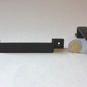 Peut inclure: Deux poignées de porte en métal noir avec des bords arrondis et une forme rectangulaire. Les poignées mesurent environ 10 cm de long et 2 cm de large. Une pièce de 2 euros est incluse pour l'échelle.