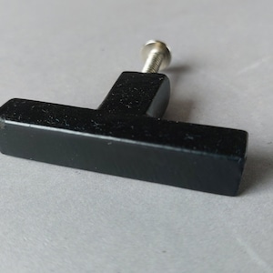 Op de afbeelding: Zwarte T-vormige kastknop met een zilveren schroef.