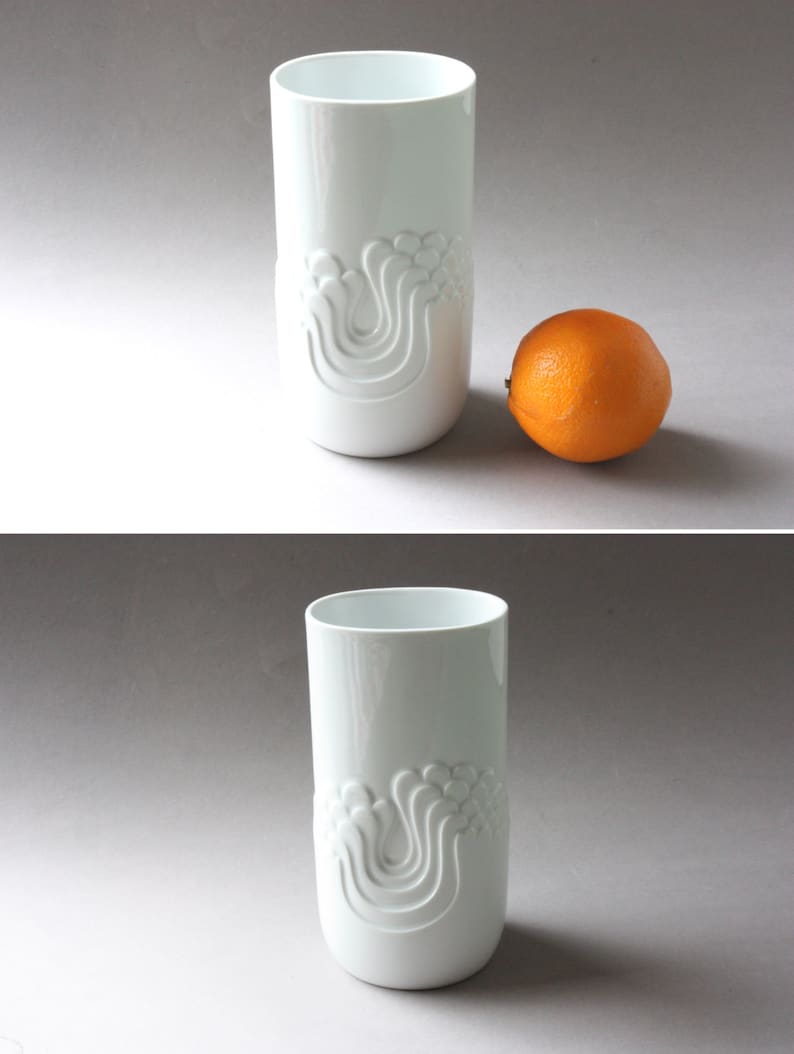May include: White ceramic vase with a raised design of stylized waves. The vase is cylindrical and has a smooth, glossy finish.