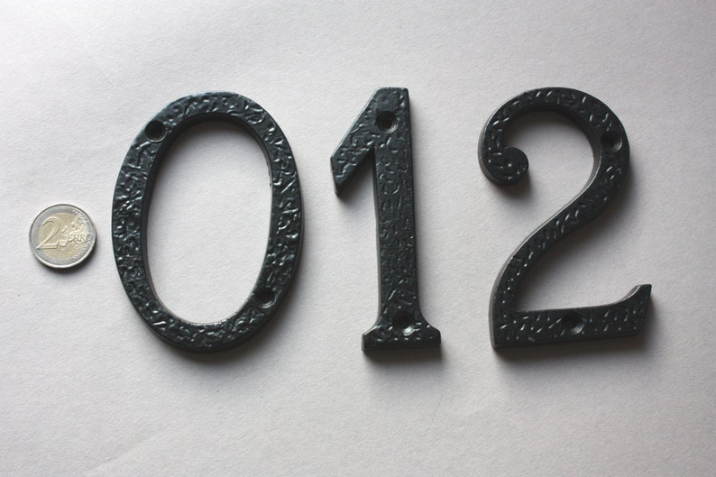 K&ouml;nnte beinhalten: Schwarze Hausnummern aus Metall 012. Die Zahlen sind in einer dekorativen Schriftart und haben eine strukturierte Oberfl&auml;che.