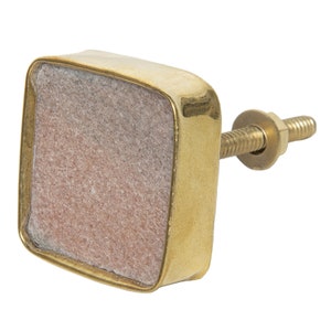 May include: Square cabinet knob with a light pink stone inset and a gold metal frame. The knob has a screw for attaching it to a cabinet door.
