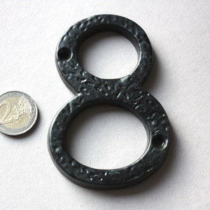 K&ouml;nnte beinhalten: Schwarze Hausnummer acht aus Metall. Die Nummer besteht aus einem einzigen St&uuml;ck Metall und hat eine strukturierte Oberfl&auml;che. Die Nummer ist etwa so gro&szlig; wie eine Zwei-Euro-M&uuml;nze.