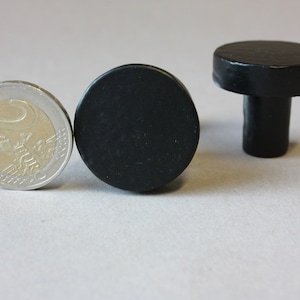 Puede incluir: Dos pomos redondos negros para armario con un tallo corto. Los pomos son aproximadamente del tamaño de una moneda de 1 euro.