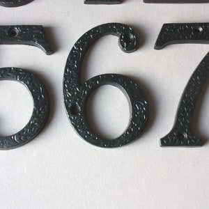 K&ouml;nnte beinhalten: Schwarze Hausnummern aus Metall 5, 6, 7 und 8. Die Zahlen haben eine strukturierte Oberfl&auml;che und sind f&uuml;r den Au&szlig;enbereich konzipiert.