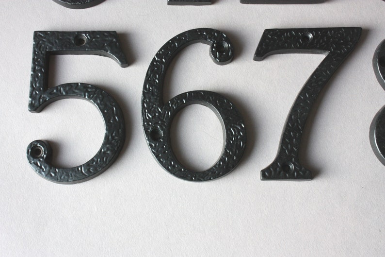 K&ouml;nnte beinhalten: Schwarze Hausnummern aus Metall 5, 6, 7 und 8. Die Zahlen haben eine strukturierte Oberfl&auml;che und sind f&uuml;r den Au&szlig;enbereich konzipiert.