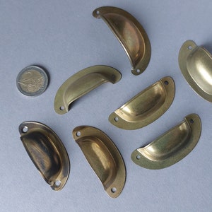 Op de afbeelding: Zeven messingkleurige metalen ladegrepen met een afgeronde, licht gebogen vorm. De grepen hebben een gladde, gepolijste afwerking.