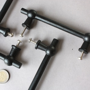 Peut inclure: Quatre poignées de porte de placard en métal noir avec des boutons ronds et des vis. Les poignées sont disposées sur une surface grise.