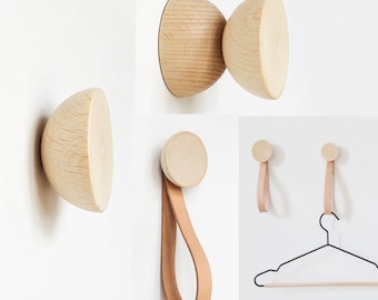 May include: Set of wooden wall hooks with leather straps. The hooks are round and have a natural wood finish. The straps are brown and are attached to the hooks with a knot. The hooks are mounted on a white wall.