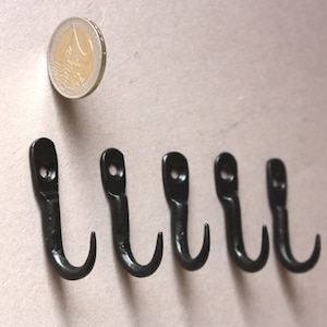 May include: Six black metal hooks with a rounded top and a curved hook. A Euro coin is shown for scale.