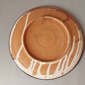 May include: The back of a terracotta plate with white painted lines and a dark blue rim.