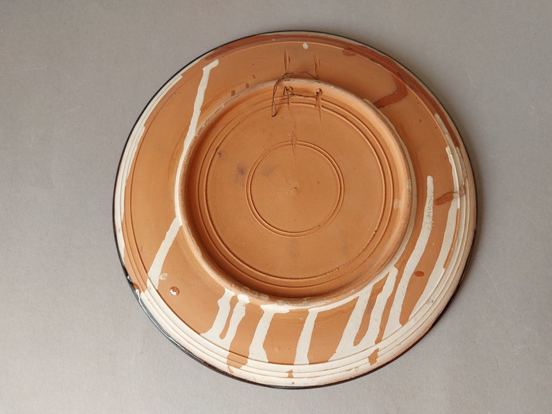 May include: The back of a terracotta plate with white painted lines and a dark blue rim.