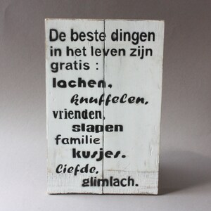 Könnte beinhalten: Weißes Holzschild mit schwarzem Text, der lautet: "De beste dingen in het leven zijn gratis: lachen, knuffelen, vrienden, slapen, familie, kusjes, liefde, glimlach."