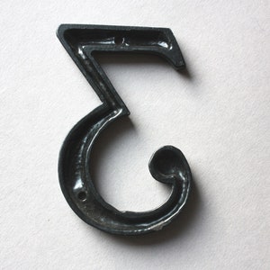 K&ouml;nnte beinhalten: Schwarze Hausnummer drei aus Metall. Die Nummer ist in einer dekorativen, geschwungenen Schriftart gestaltet.