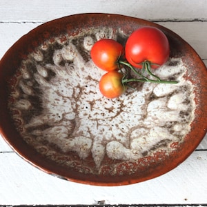 Könnte beinhalten: Eine braune Keramikschale mit einer weißen und braunen Marmorierung. Drei rote Tomaten sind in der Schale angeordnet.