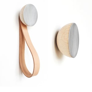 Op de afbeelding: Twee houten wandhaken met een zilveren metalen afwerking. Eén haak heeft een leren lus.