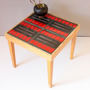 May include: A square wooden end table with four legs. The table top is covered in red and black patterned tiles.