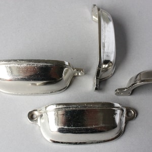 Könnte beinhalten: Vier silberne Schubladengriffe für Schränke. Zwei sind gebogen und zwei sind rechteckig.