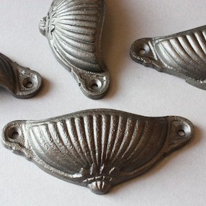 May include: Four cast iron drawer pulls with a scalloped design. The pulls are a dark gray color and have a slightly distressed finish.