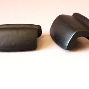 Könnte beinhalten: Zwei mattschwarze Schrankknöpfe. Einer ist rechteckig, der andere hat ein geschwungenes Design. Beide haben ein glattes, solides Aussehen. Diese Knöpfe sind wahrscheinlich für Möbel oder Schränke.