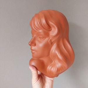 May include: A terracotta bust of a woman with long, flowing hair. The bust is in profile, and the woman's face is serene.