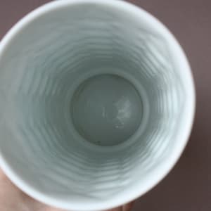 以下が含まれることがあります： 織り模様の入った白い陶器の花瓶。花瓶は空で、上部に丸い開口部があります。