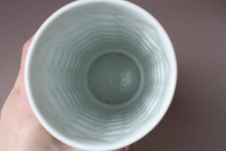 以下が含まれることがあります： 織り模様の入った白い陶器の花瓶。花瓶は空で、上部に丸い開口部があります。