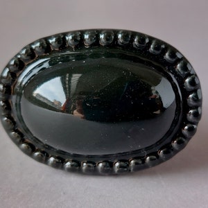 Könnte beinhalten: Schwarzer ovaler Schrankknopf mit einem perlenbesetzten Rand.