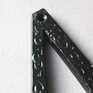 K&ouml;nnte beinhalten: Nahaufnahme eines schwarzen Metalldreiecks mit einem dekorativen Muster. Das Dreieck hat ein kleines Loch oben.