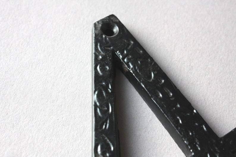 K&ouml;nnte beinhalten: Nahaufnahme eines schwarzen Metalldreiecks mit einem dekorativen Muster. Das Dreieck hat ein kleines Loch oben.