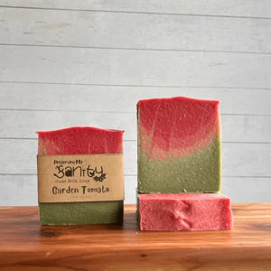 May include: Two bars of handmade goat milk soap, one stacked on top of the other. The top bar is red and green with a swirl pattern. The bottom bar is red. Both bars have a label that reads "Preserving My Sanity Goat Milk Soap Garden Tomato".